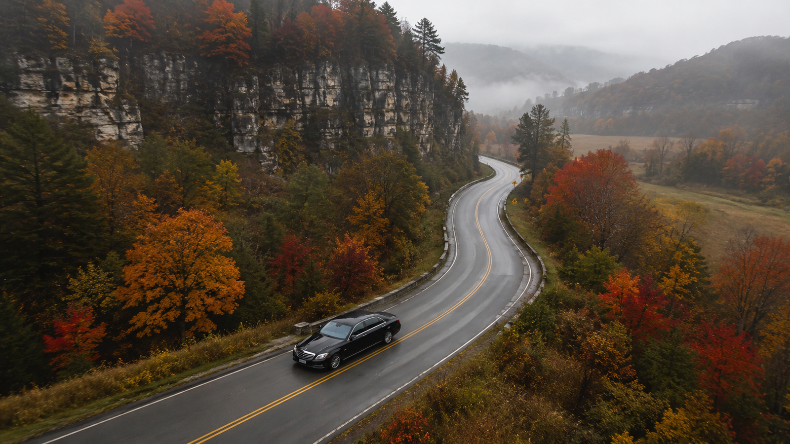 Navy blue luxury sedan limo driving through a winding valley road in Chatsworth during autumn.
