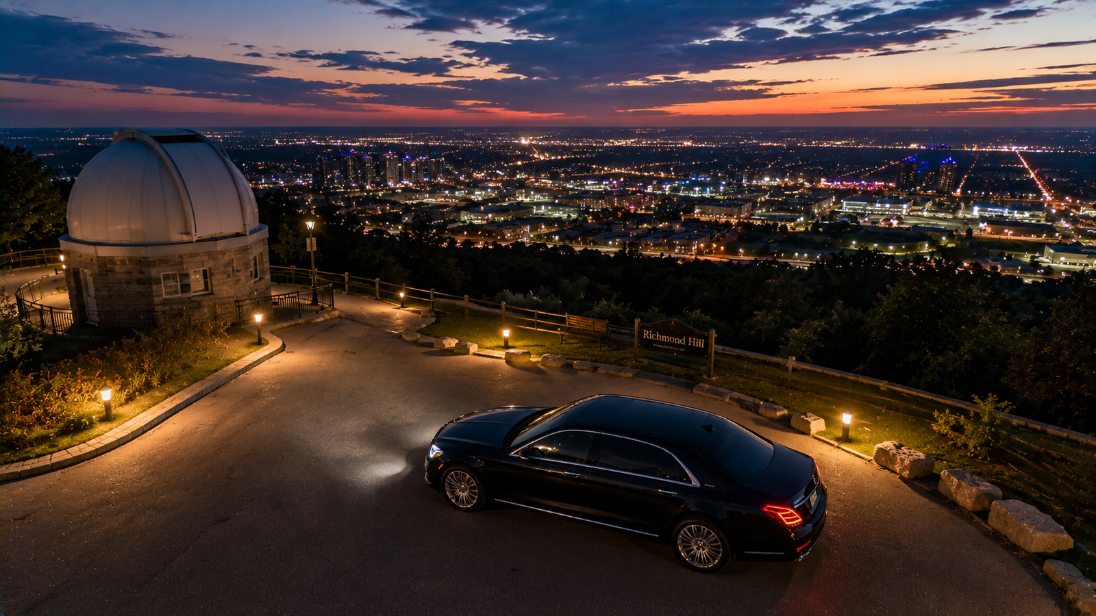 Black executive sedan limo parked on an observatory hill overlooking Richmond Hill at dusk.